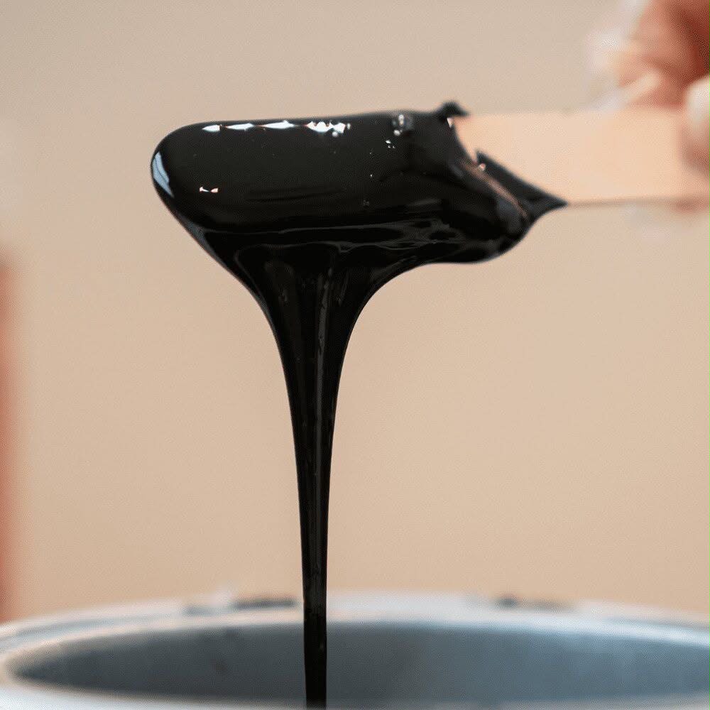 Black wax dripping from a wooden waxing applicator