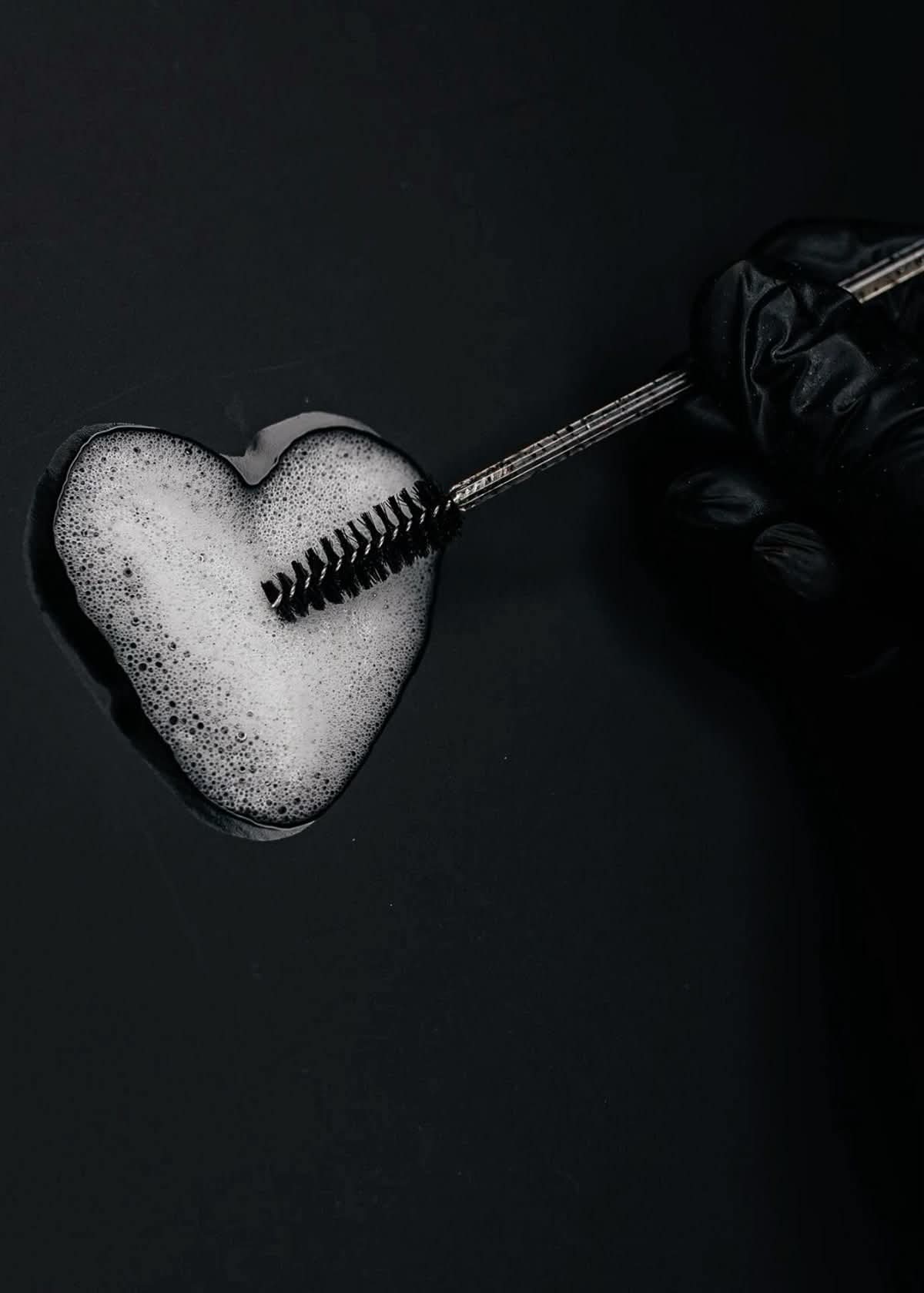 Lash spoolie resting over a heart-shaped bowl of cleansing foam